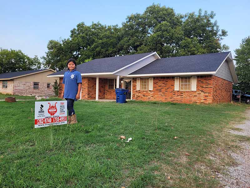Front view of a small residential home recently worked on by Lira Roofing, with the company's yard sign in front