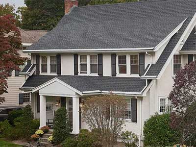 Front view of a mid-class, light beige home with gray GAF shingles on its roof