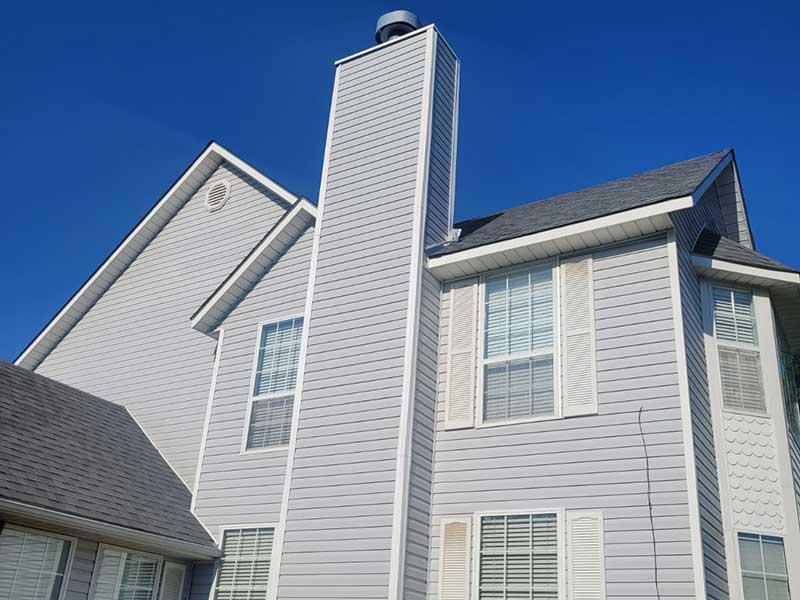 Side view of a large home with new light gray siding installed by Lira Roofing